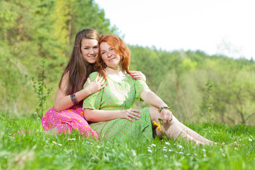 funny mother and daughter sitting on green grass