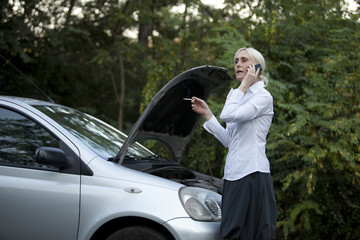 woman besides her broken car smoking and talking on the cell pho
