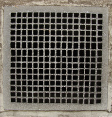irregular metal grid from a ventilation shaft in a concrete wall