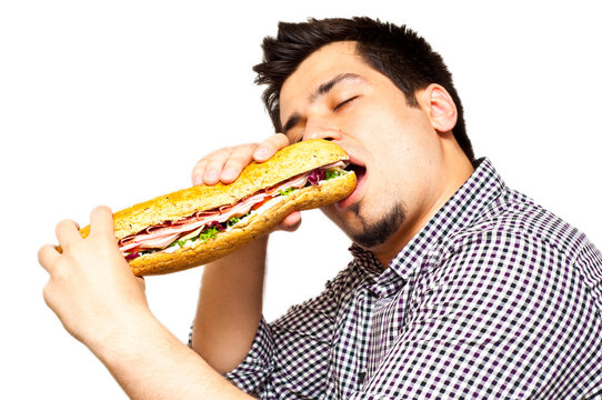 Young Man Eating A Freshly Made Sub Meat Feast Sandwich