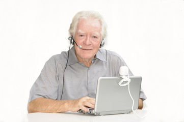 Älterer Herr mit Netbook, Webcam und Headset