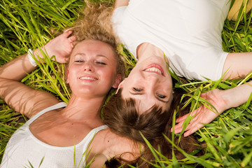 Two beautiful young women lay on green grass outdoors