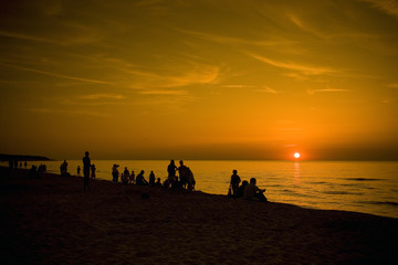 Ludzie obserwujący zachód słońca nad morzem bałtyckim - obrazy, fototapety, plakaty