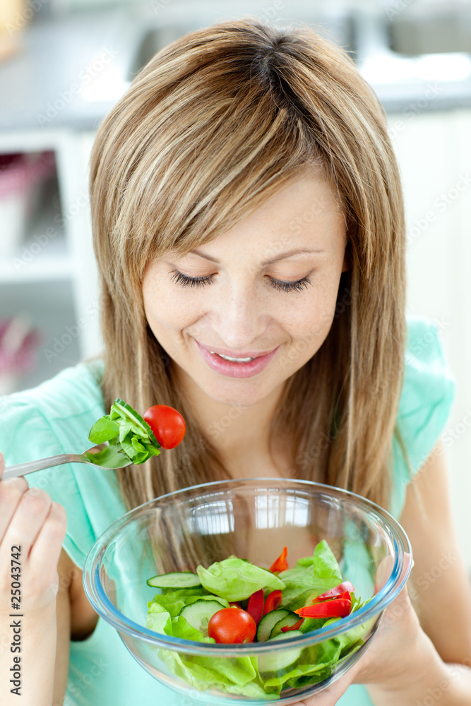 Wall mural Cute young woman eating a healthy salad in the kitchen