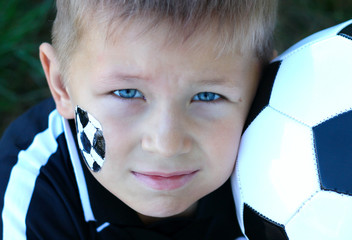 A young boy with painted face and soccer ball.