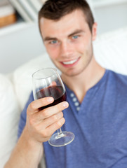 Charismatic young man holding a glass of wine sitting on a sofa