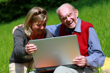 Alter Mann und junge Frau lachend am Laptop im Grünen