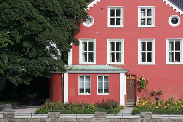 a red big house  with many windows, trees and flowers in a charming  neighborhood of a  calm town