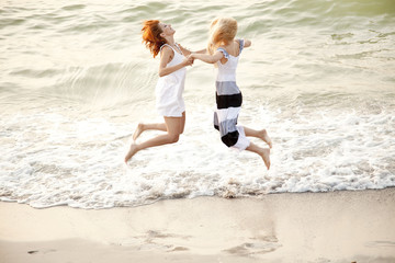 Fototapeta premium Two beautiful young girlfriends jumping on the beach