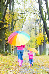 mother and her daughter with umbrellas in autumnal alley