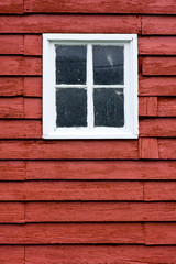 Close up square white window in old red wooden barn wall.