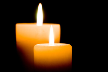 Close up of two lit white candles on black background.