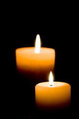 Close up of two lit white candles on black background.