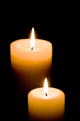 Close up of two lit white candles on black background.