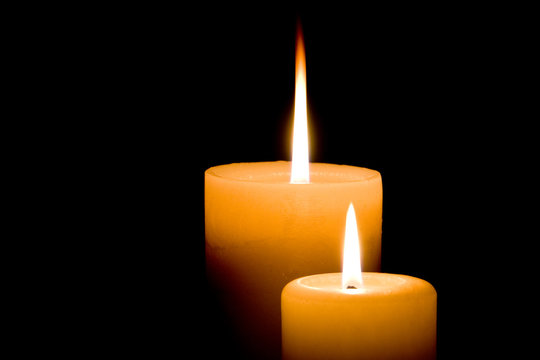 Close up of two lit white candles on black background.