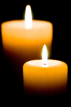 Close up of two lit white candles on black background.