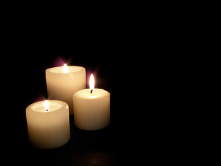 Fototapeta na wymiar Close up of three lit candles on black background.