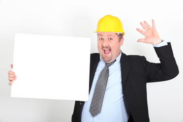 Homme en costume et casque de chantier avec un panneau blanc