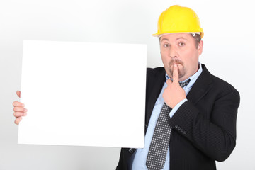 Homme en costume et casque de chantier avec un panneau blanc