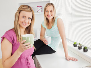 Portrait of two happy women holding cups of coffee at home