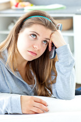 Bored young woman holding a  remote sitting in the kitchen