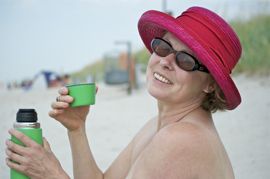Frau am Strand sitzend mit gr&uuml;ner ge&ouml;ffneter Thermoskanne
