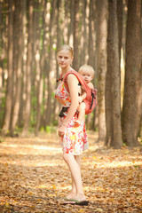 mother carrying daughter in sling in forest