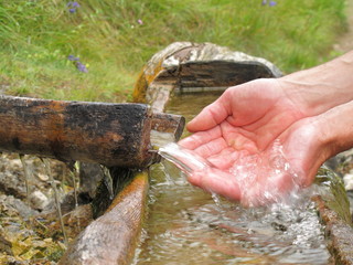 Hände schöpfen Wasser am Brunnen bei Wanderung
