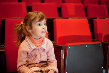 Smiling little girl sitting on armchairs at cinema