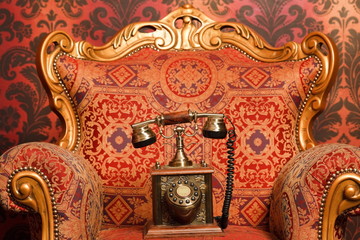 old phone is chair with gold accents, vintage wallpaper.