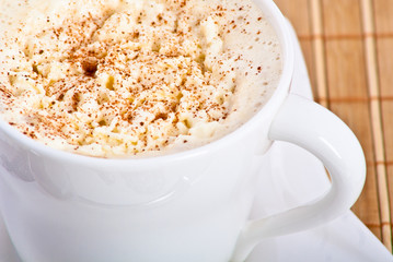mug of coffee with whipped cream and cinnamon on bamboo mat