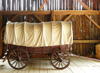 Covered wagon in a sunlit rustic barn - obrazy, fototapety, plakaty