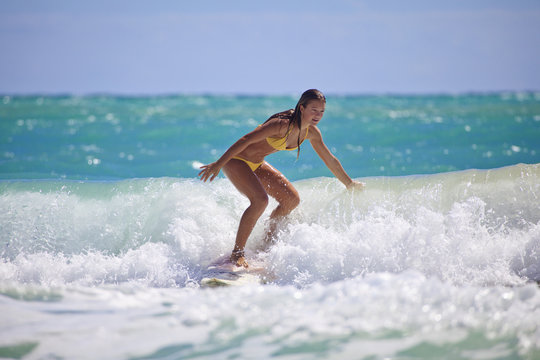 teenage girl in a yellow bikini surfing in Hawaii