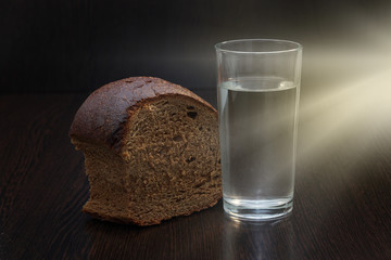 Bread, water and sun beam on wooden background.