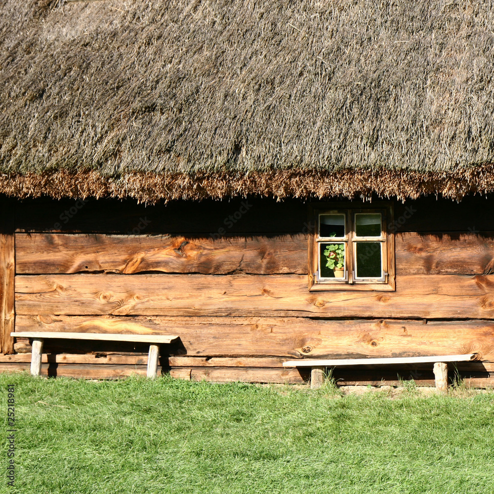 Wall mural Antique house with a thatched roof and benches in front of it