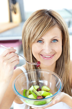 Portrait of a radiant woman eating a fruit salad in the kitchen