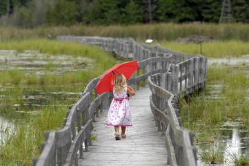 Little blond girl with red umbrella on boardwalk