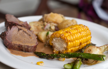Cuts of veal with sauce and corn some aspargus up front
