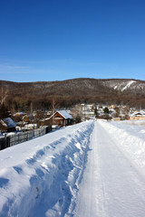 Fototapeta na wymiar Winter village road against mountains and a blue sky