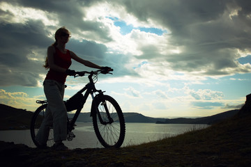 Silhouette of the girl with a bicycle against mountains