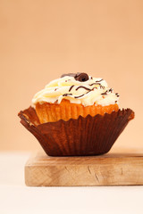 cupcake with lemon icing partly unwrapped on wooden board