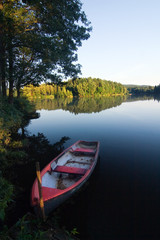 Obraz premium Evening summer countryside with pond, boat, forest and blue sky