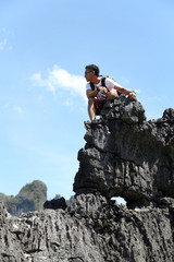 A man hiking with a bag on his back celebrates on top of a rock with his hands raised in triumph