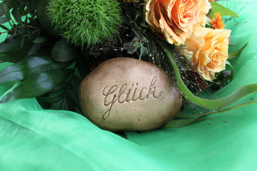 Stein mit der Inschrift Glück vor einem Blumenstrauß