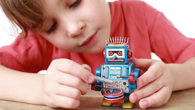 girl in T-shirt knocks winder on drum of clockwork toy robot