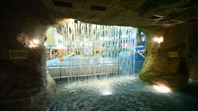Through waterfall of stone cave seen people bathing in pool