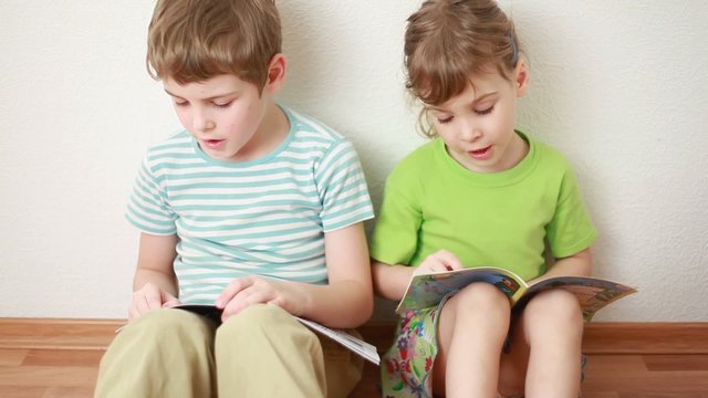 boy and girl sit leaning against wall and read children's books