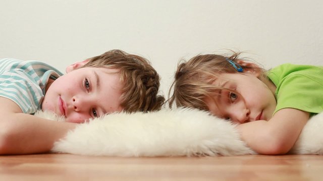 boy and little girl  lie on wooden floor on shaggy carpet