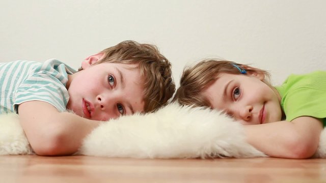 boy and little girl  lie on wooden floor on shaggy carpet