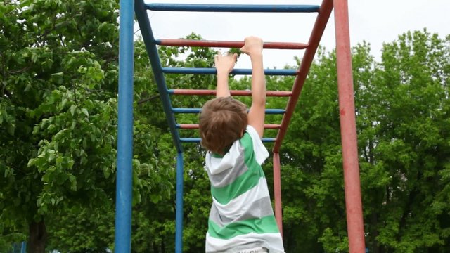 boy in shirt climbs down wall bars like monkey on playground
